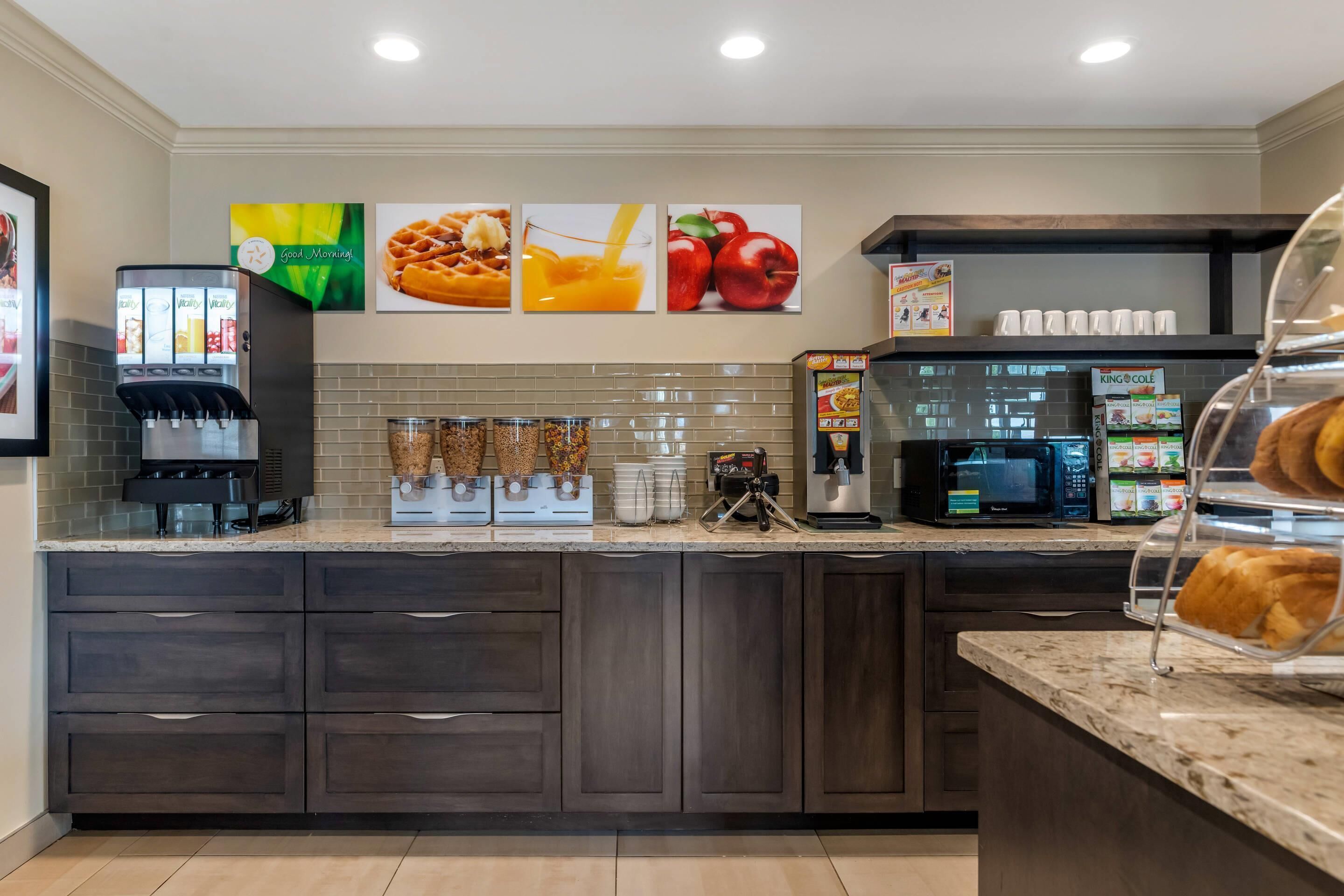 A kitchen area with a coffee machine, microwave, and a display case with pastries.