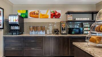 A kitchen area with a coffee machine, microwave, and a display case with pastries.