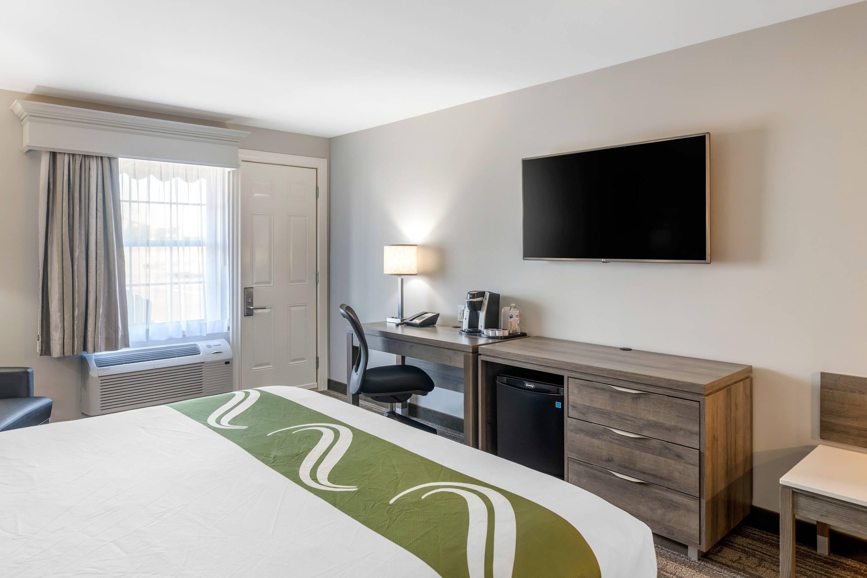 A hotel room with a bed, desk, chair, TV, and a window with curtains.