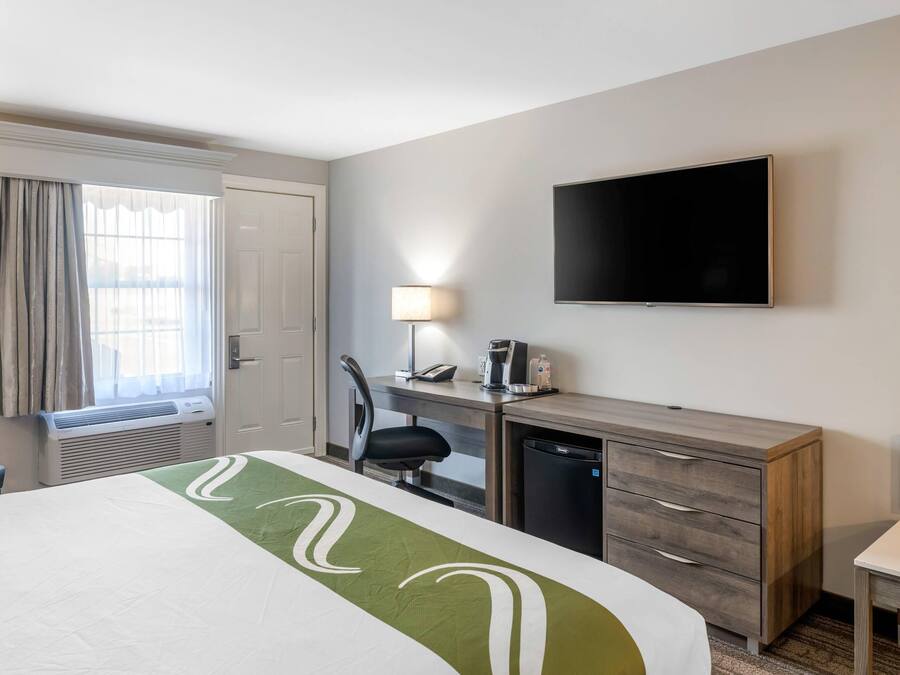 A hotel room with a bed, desk, chair, TV, and a window with curtains.