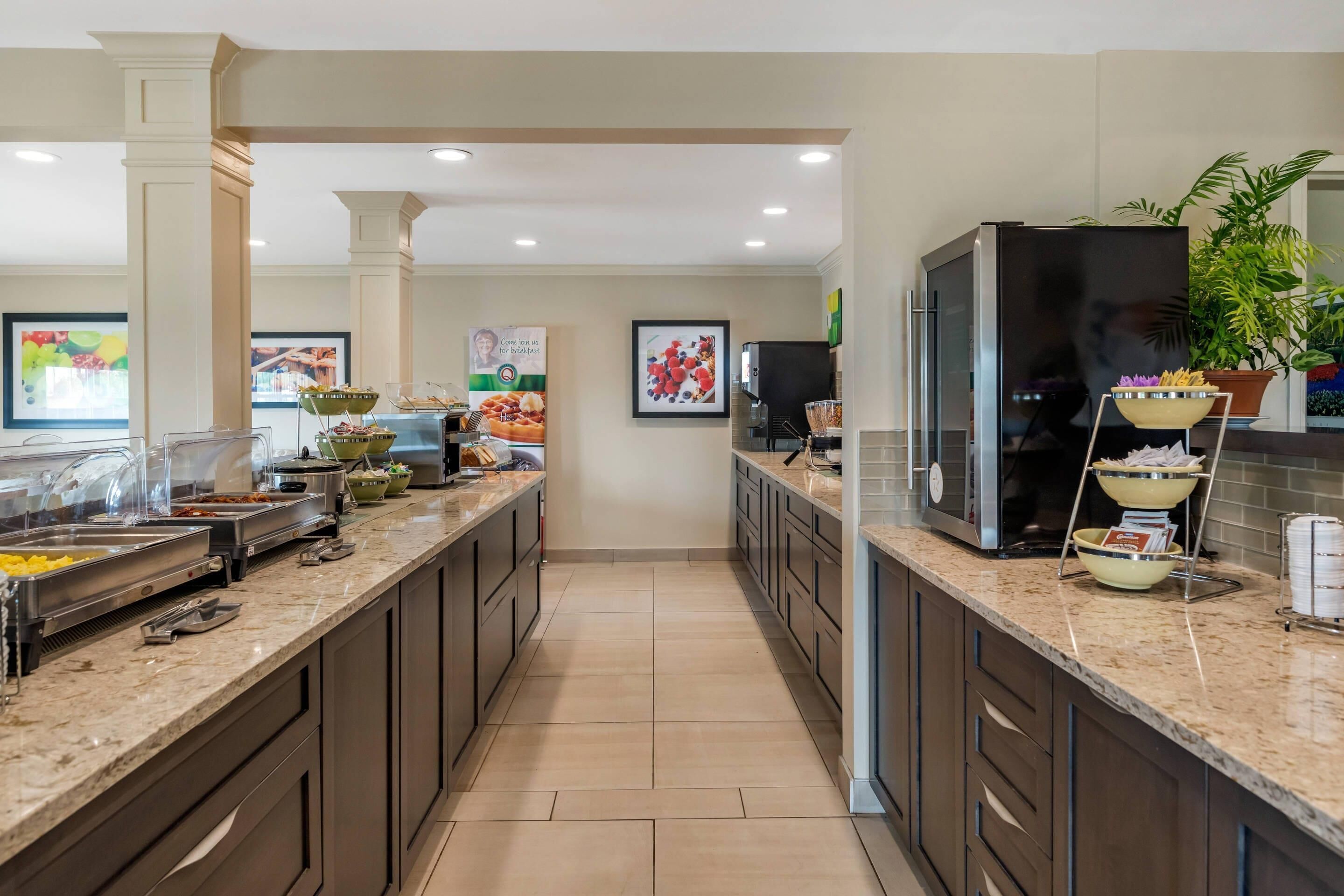 A modern kitchen with granite countertops, stainless steel appliances, and a central island with a bowl of fruit.