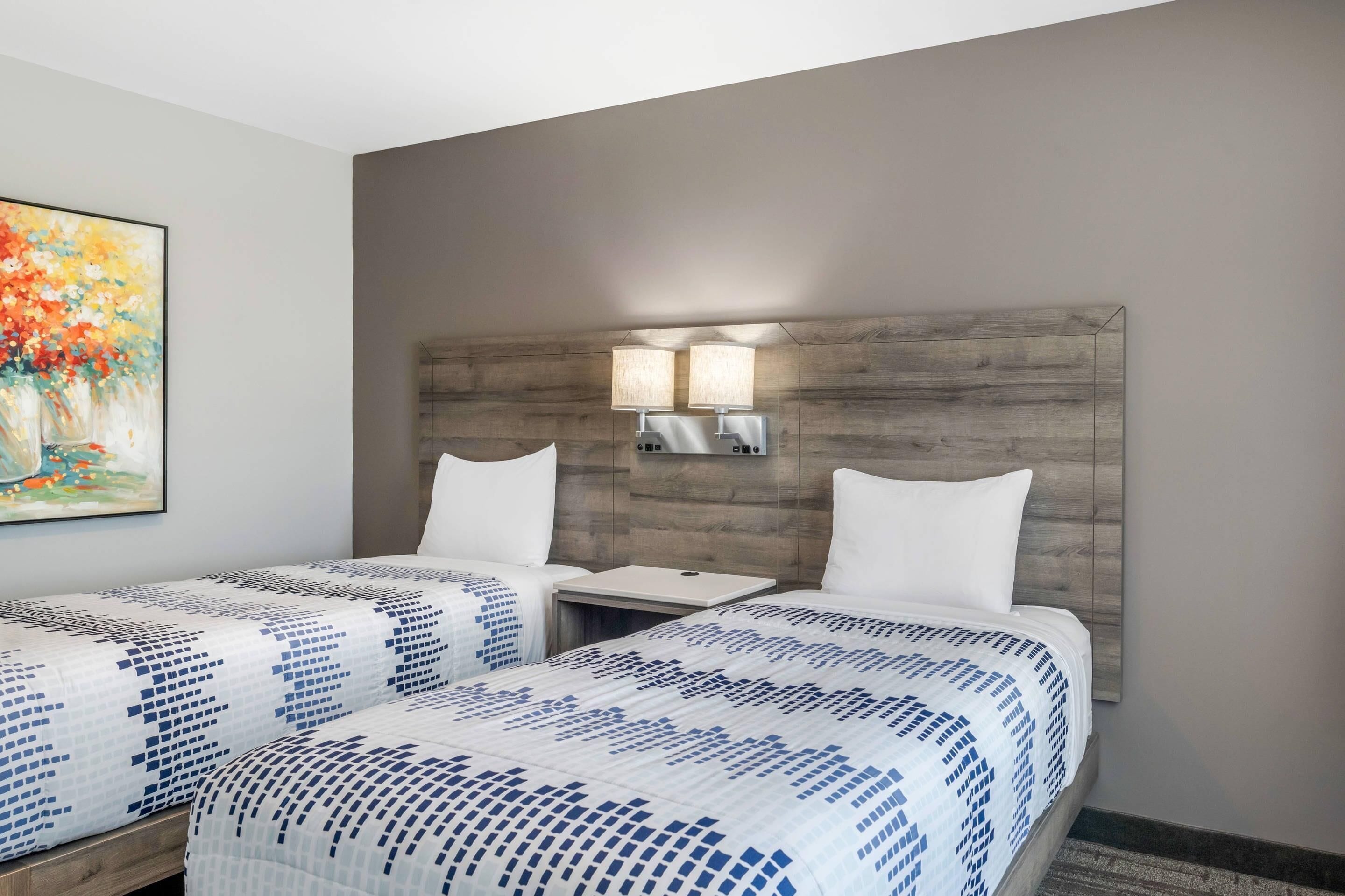 Habitación de hotel con dos camas, cabecero de madera, un cuadro en la pared y dos lámparas de pared.