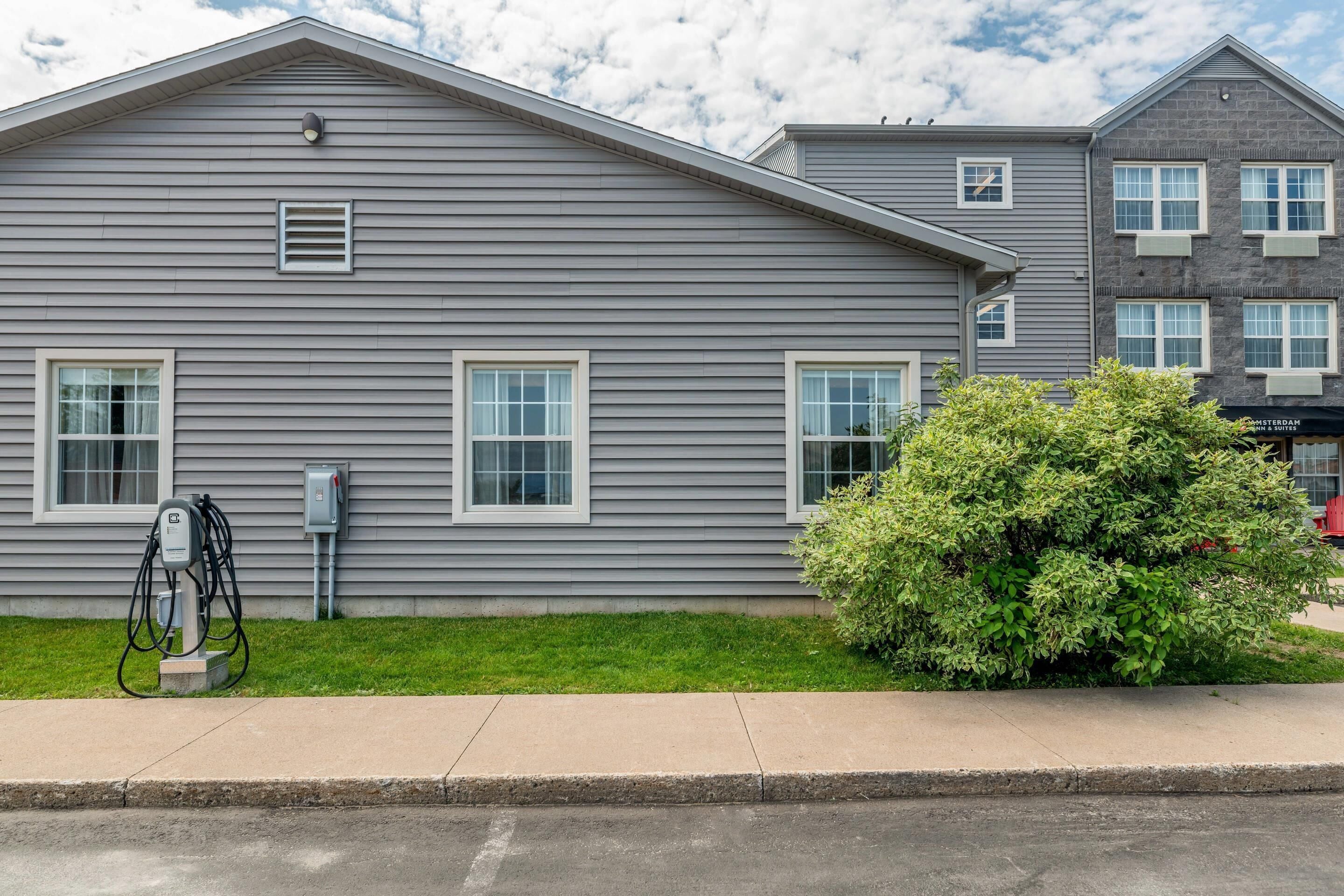 A residential building with a gray exterior, a visible electrical box, and a green bush in front.
