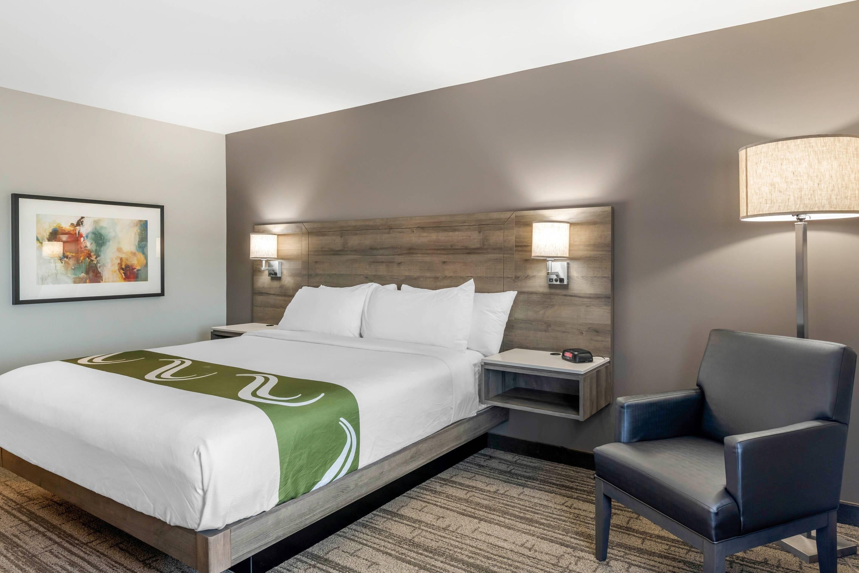 A hotel room with a large bed, two bedside tables, a chair, and a wall-mounted lamp.