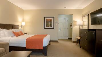 A hotel room with a bed, bedside table, lamp, dresser, and a TV mounted on the wall.