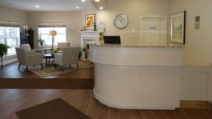 Un área de recepción moderna con un mostrador curvo, un reloj y un espacio de espera con sillas y una mesa.