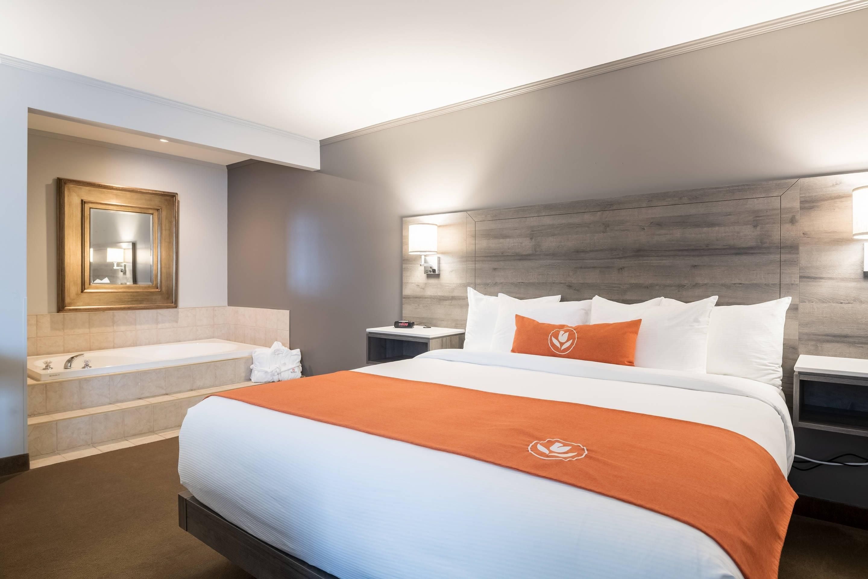 A hotel room with a large bed, a bathtub, a mirror, and a nightstand with a lamp.