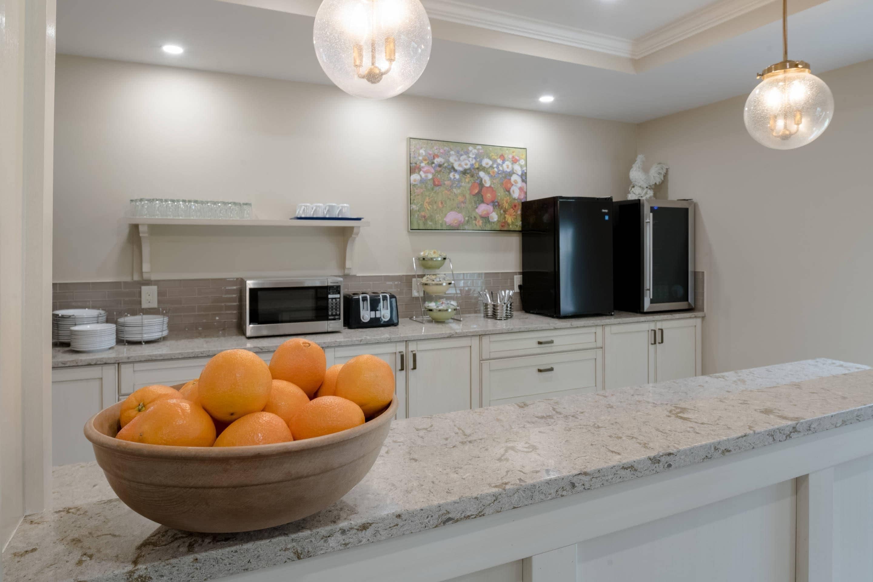 A kitchen with white cabinets, a microwave, a toaster, a bowl of oranges, and two black refrigerators.