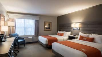 Habitación de hotel con dos camas, un escritorio, una silla, una lámpara, un cuadro en la pared y una ventana con cortinas.