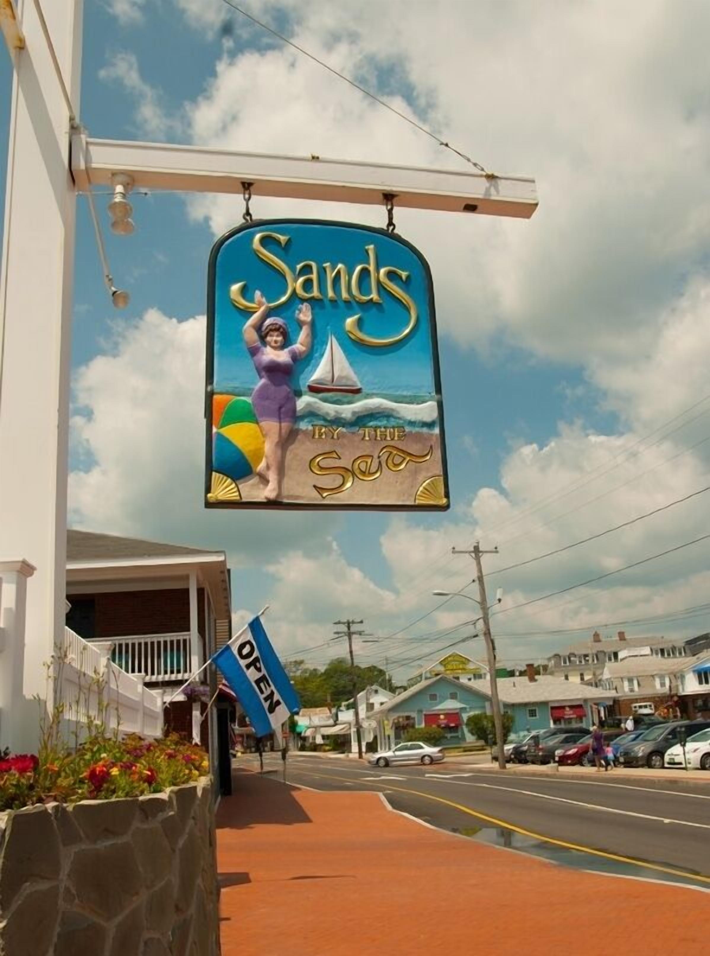 A sign for 'Sands by the Sea' with a beach scene, a sailboat, and a woman in a swimsuit.