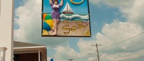 A sign for 'Sands by the Sea' with a beach scene, a sailboat, and a woman in a swimsuit.