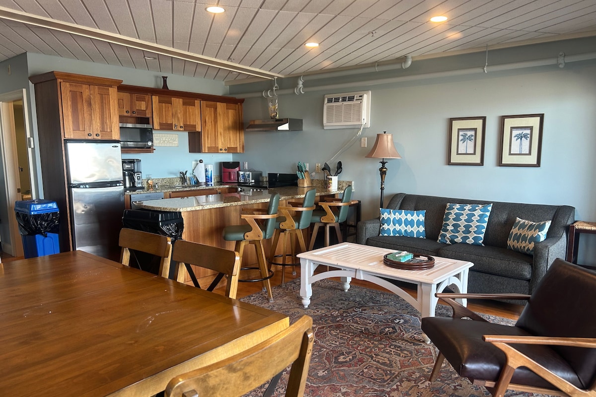 A modern kitchen with wooden cabinets, a stainless steel refrigerator, and a dining area with a wooden table and chairs.