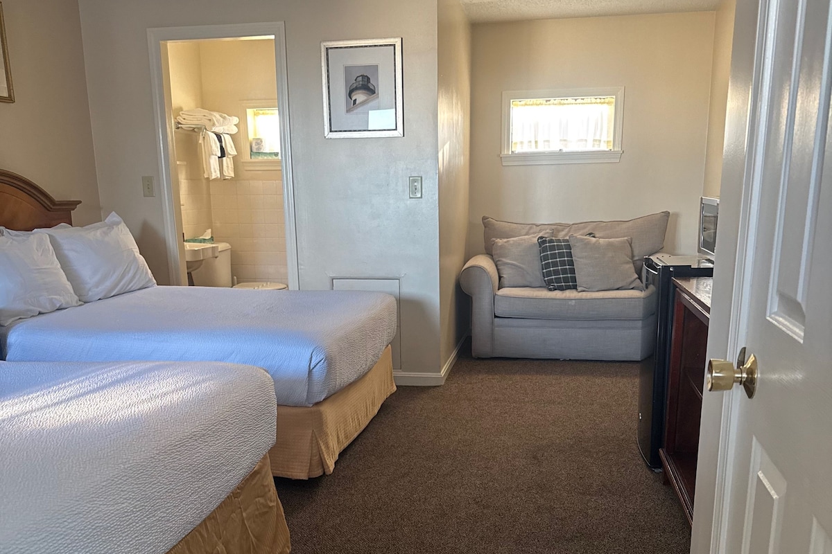 A hotel room with two beds, a sofa, a small table, and a door.