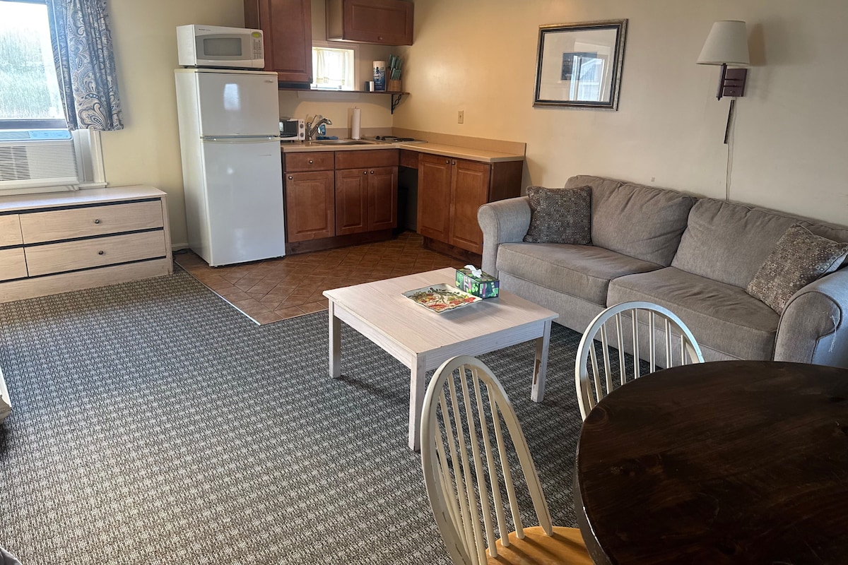 A compact living space with a kitchenette, a sofa, a dining table, and a window.