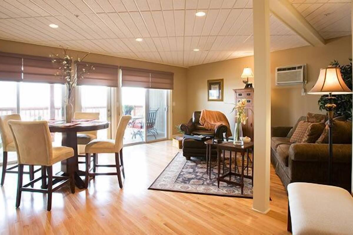 A spacious living area with a dining table, chairs, a sofa, and a coffee table. There is a large window providing natural light and a view of the outdoors.