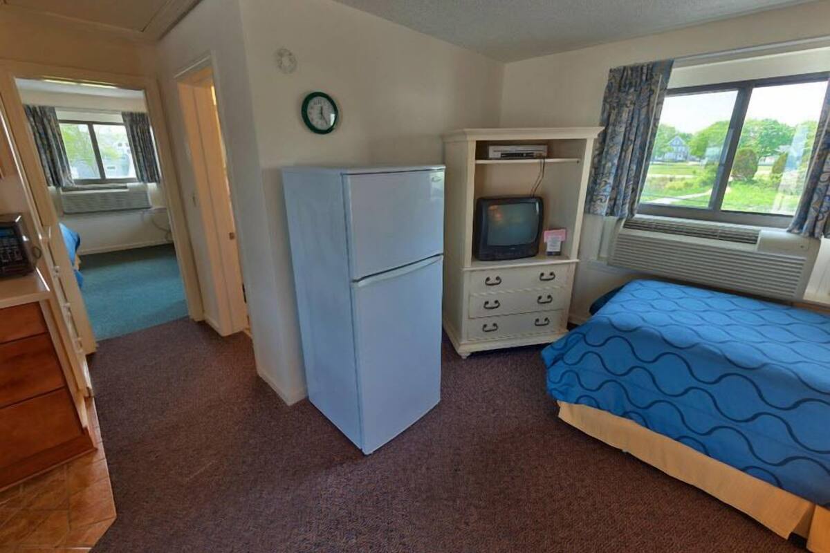 A compact room with a bed, a small refrigerator, a television, and a window with curtains.