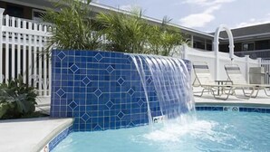A swimming pool with a blue tiled waterfall feature, surrounded by a white fence and lounge chairs. - Sands by the Sea Motel (York Beach)