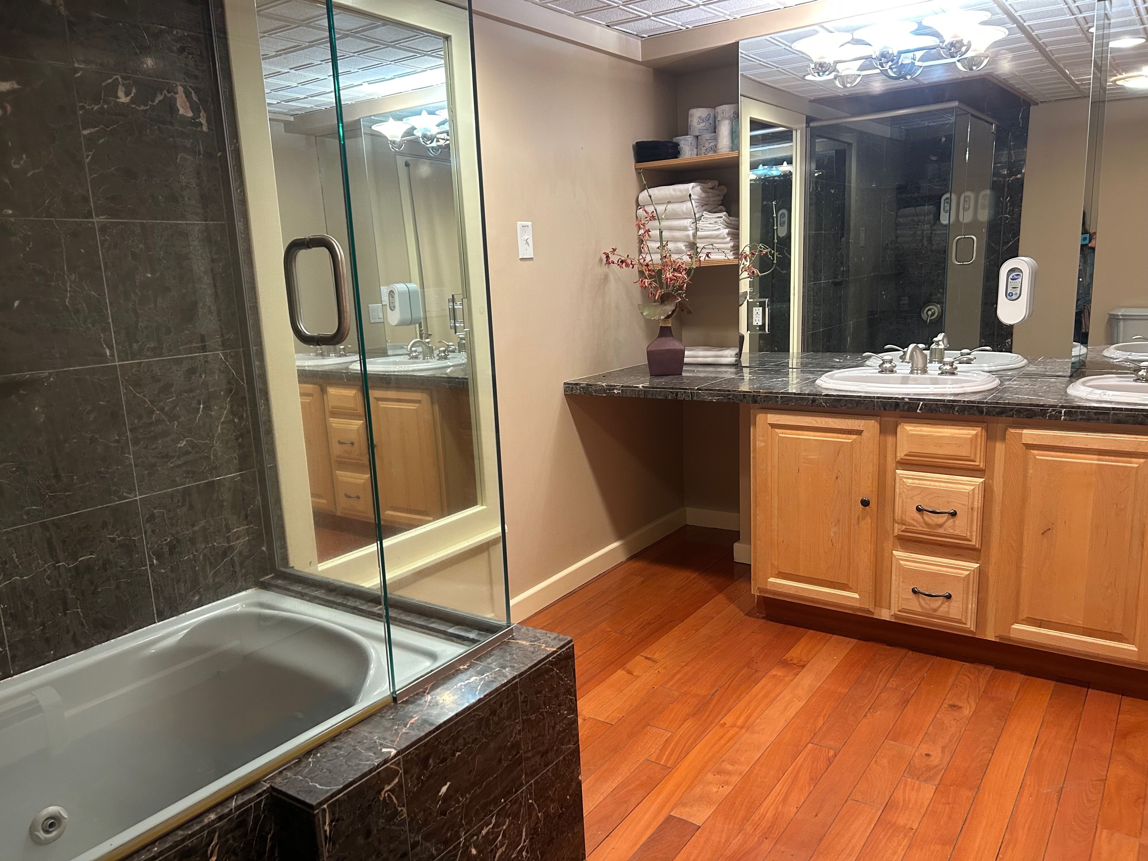 A modern bathroom with a glass-enclosed shower, wooden cabinets, and a marble countertop.