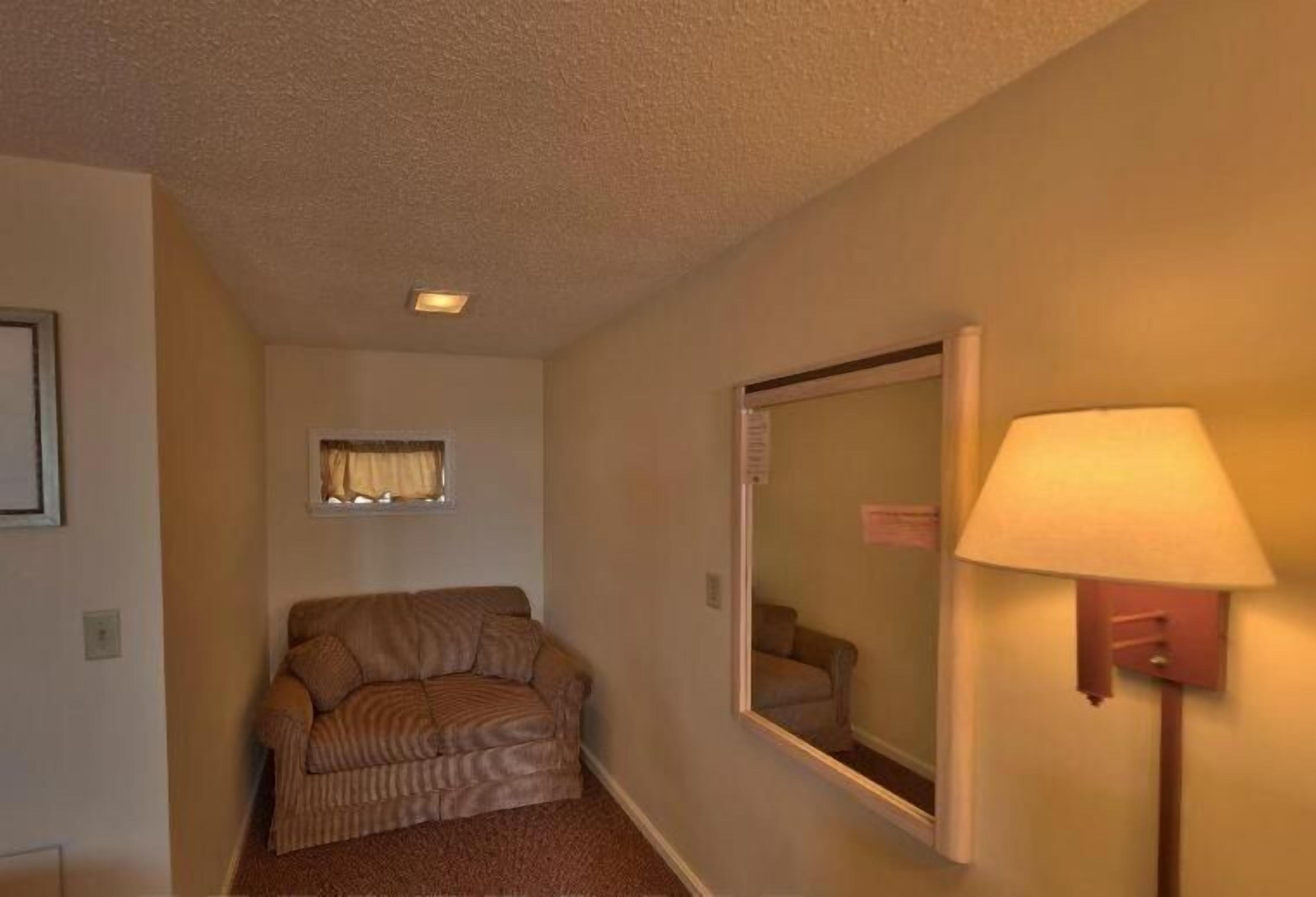 A small, carpeted room with a sofa, a wall-mounted mirror, and a floor lamp.