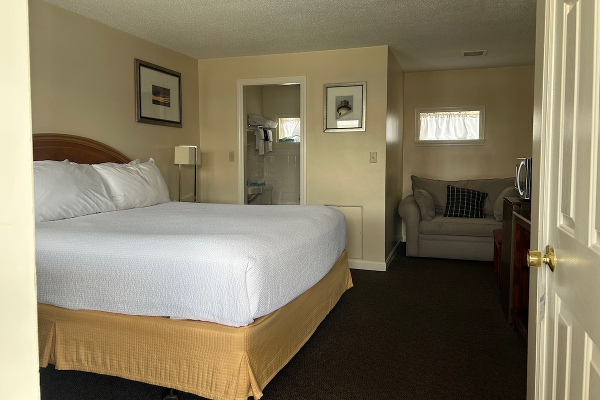A hotel room with a bed, a sofa, a bathroom, and a door.