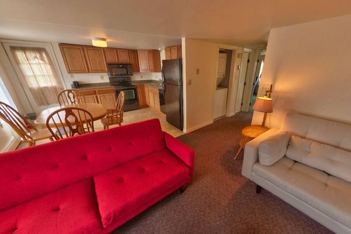 A living room with a red sofa and a white sofa, a kitchen with wooden cabinets and a refrigerator, and a dining area with chairs and a table.