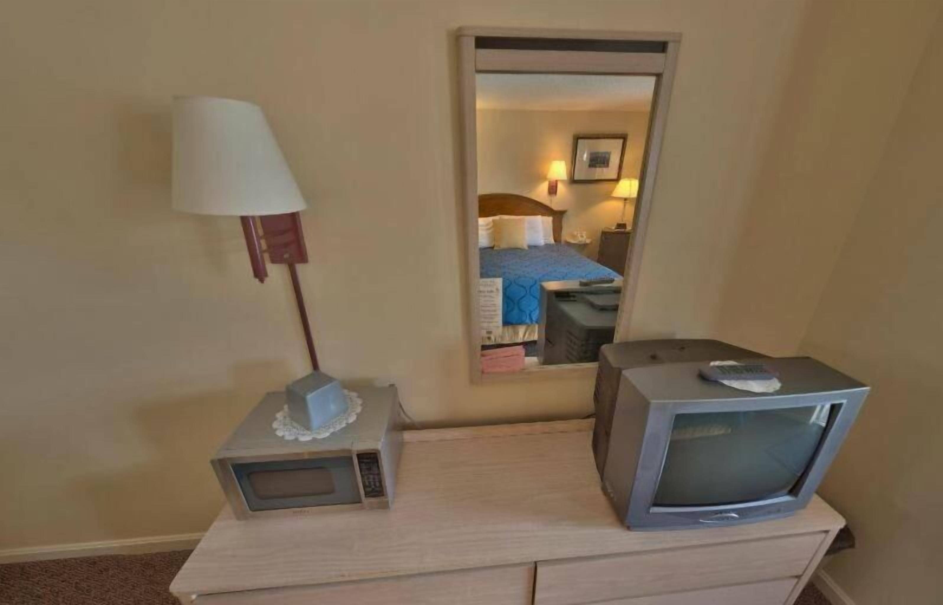 A hotel room with a bed, a bedside table with a lamp, a television, and a mirror.