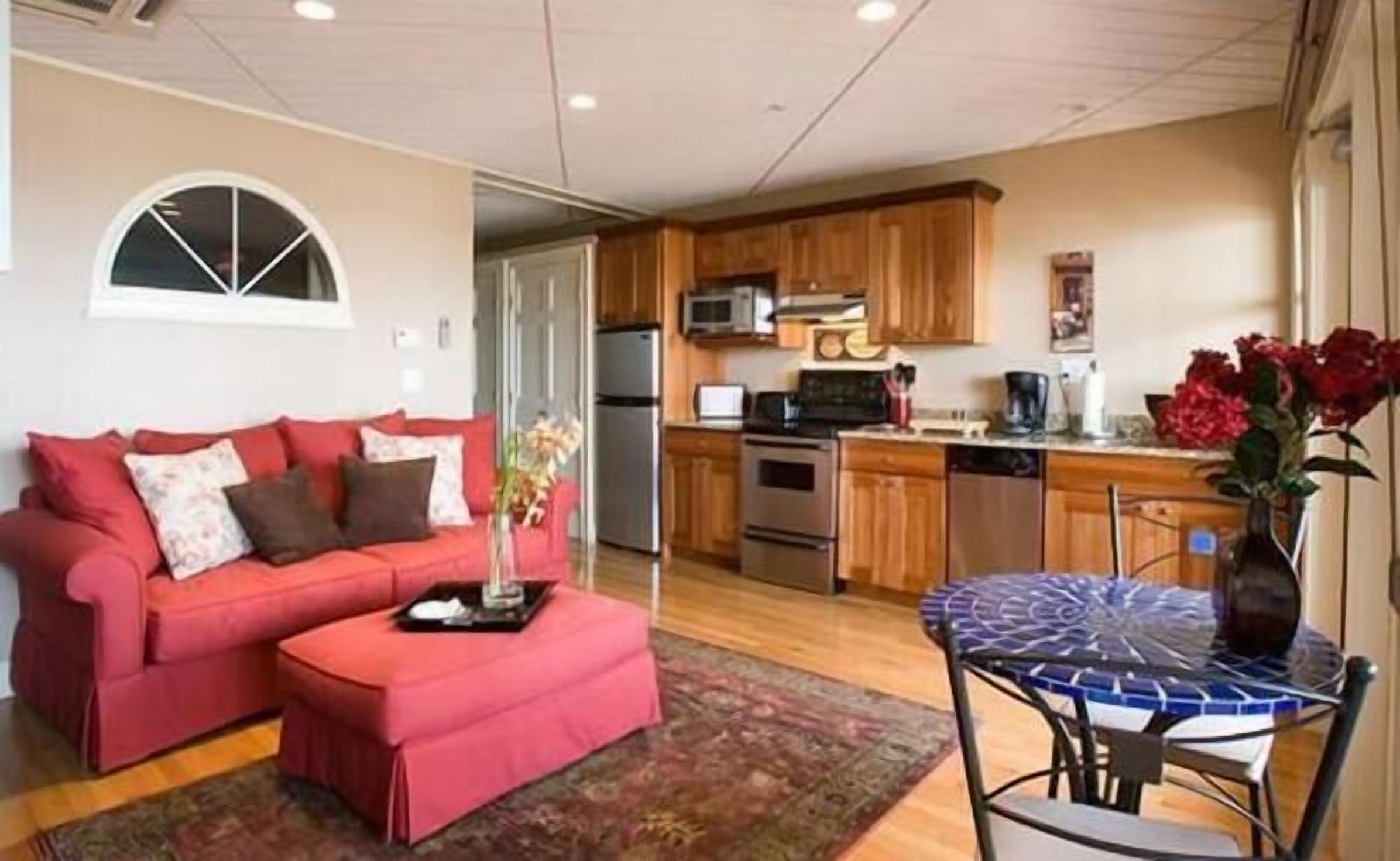 Un espacio habitable compacto con kitchenette, un sofá rojo, una mesa de centro y una zona de comedor con mesa de vidrio.