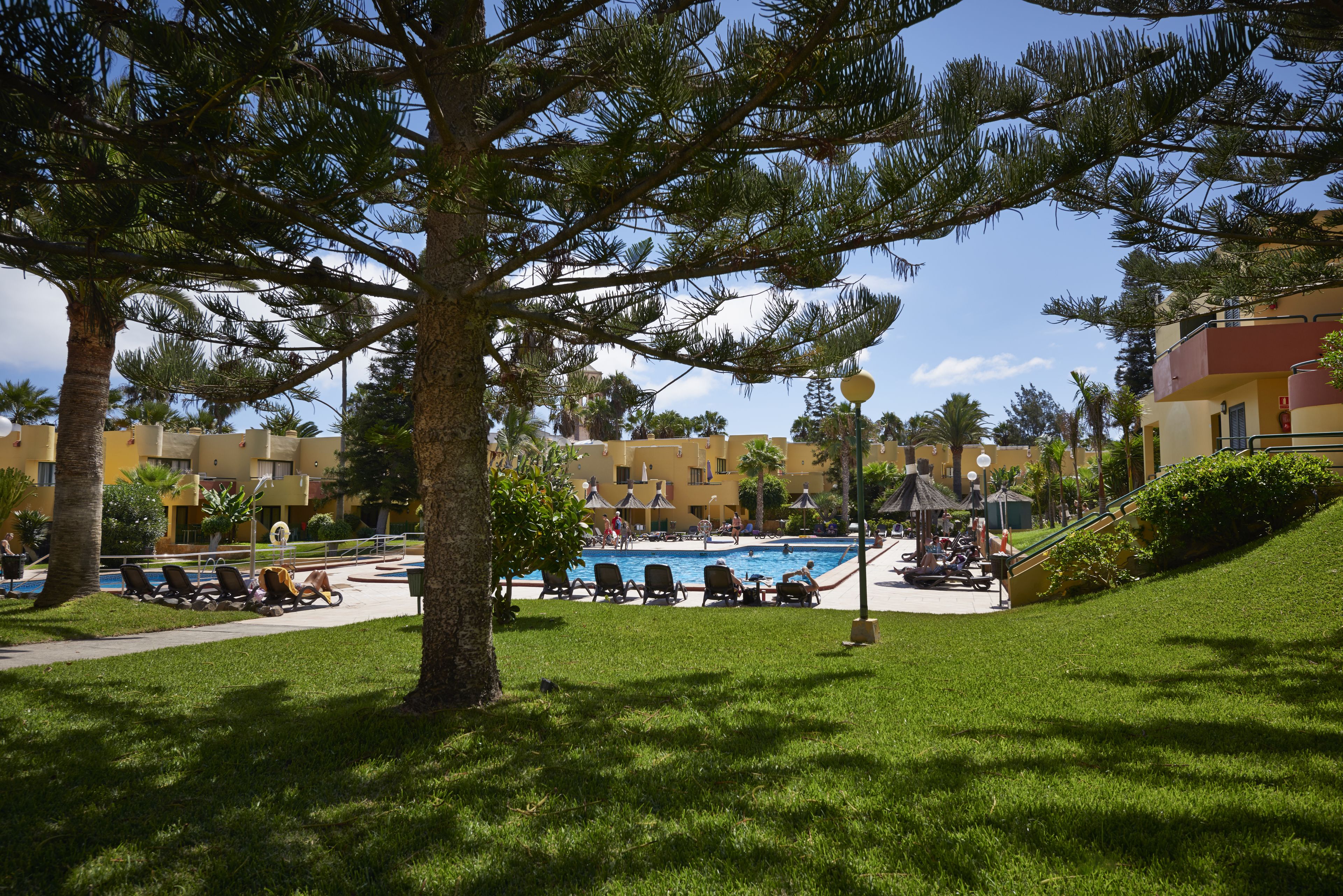 A pool area with lounge chairs, a gazebo, and a building with balconies in the background.
