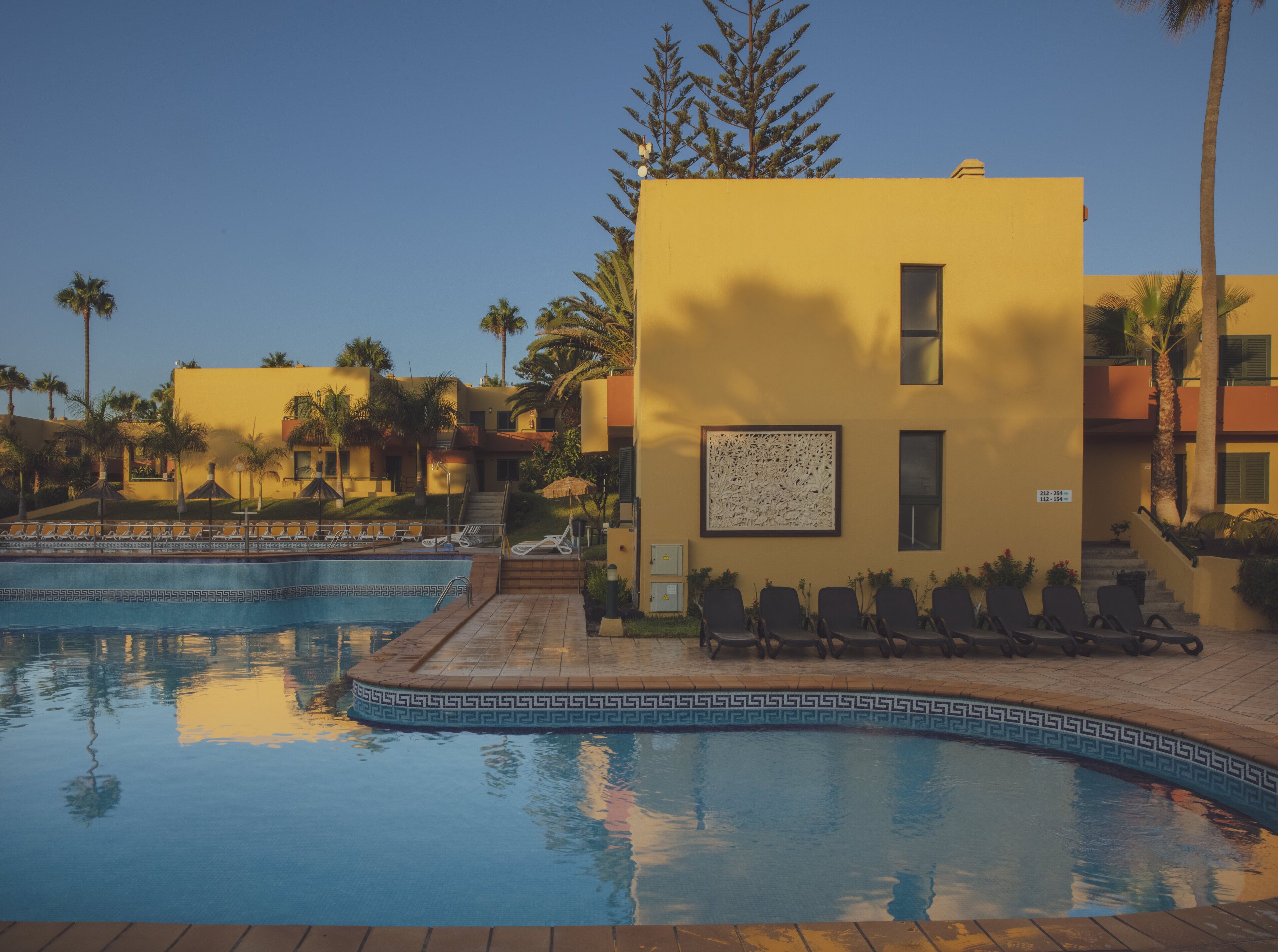 A pool area with lounge chairs, a small pool, and a building with a decorative wall.