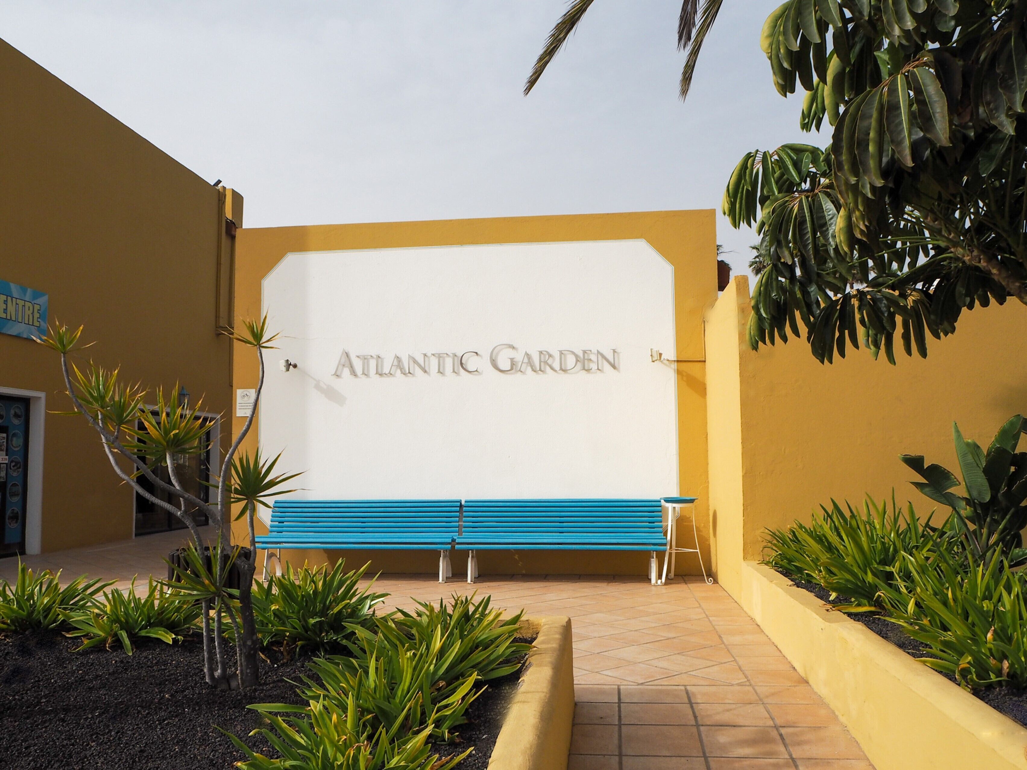 Ein Schild mit der Aufschrift 'Atlantic Garden', davor eine Bank und Pflanzen.