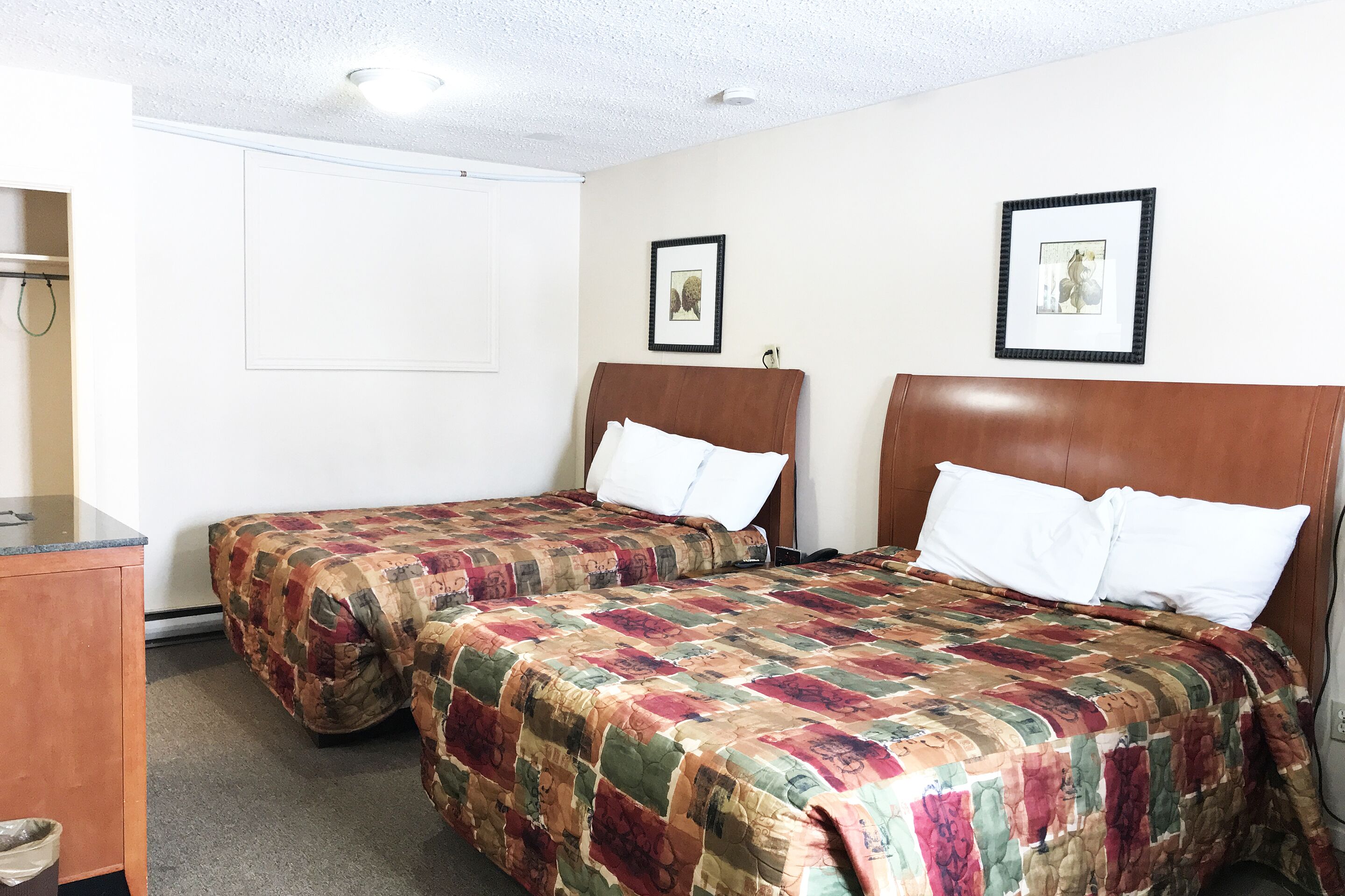 A hotel room with two single beds, a wooden headboard, a desk, and a trash bin.