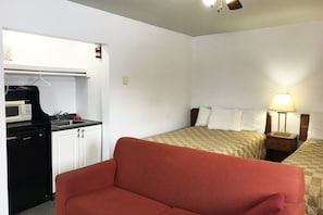 A compact hotel room with a kitchenette, a single bed, a red sofa, and a bedside lamp. - Bayside Motel (Quinte West)