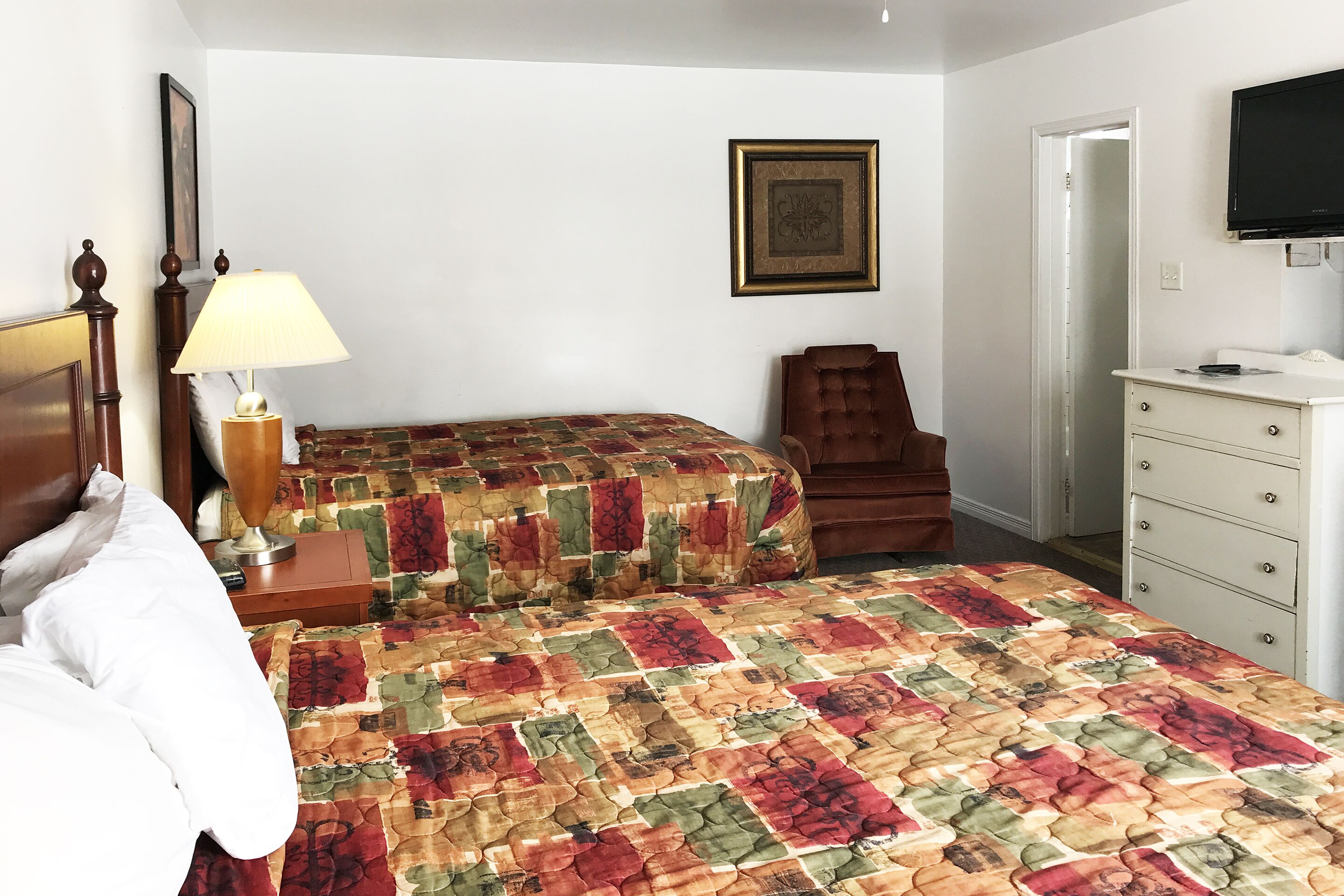 Ein Schlafzimmer mit Bett, Nachttisch, Lampe, Sessel, Kommode und Fernseher.