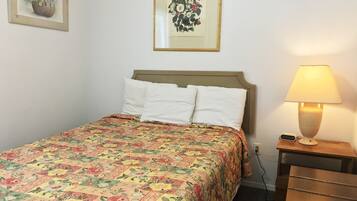 Een netjes opgemaakt bed met een bloemenbedekking, een bedlampje en een klein tafeltje met een lamp.
