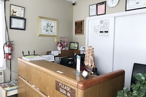 A reception desk with a 'Please Sign In' sign, framed certificates, a clock, and a 'No Smoking' sign. - Bayside Motel (Quinte West)