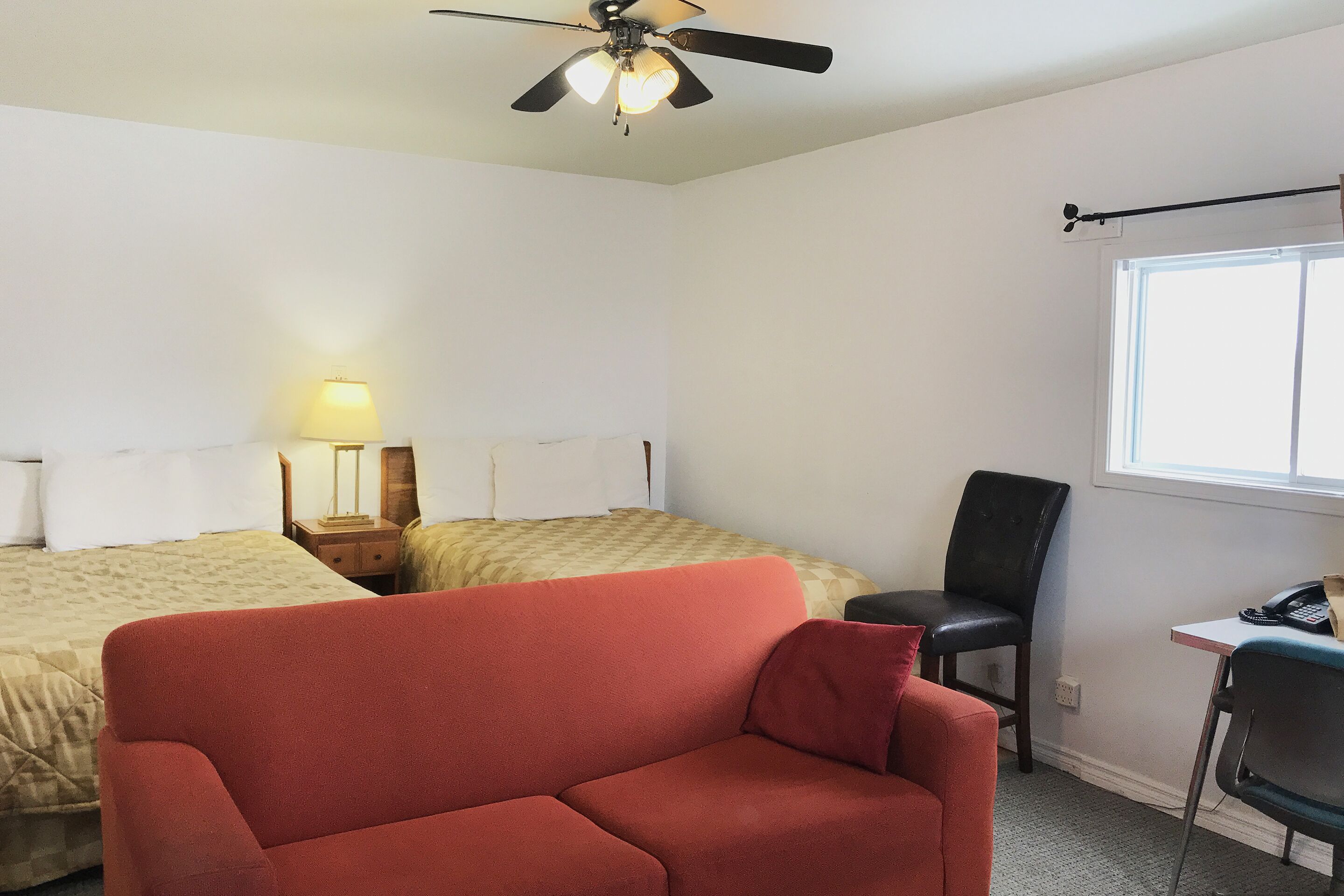 Une chambre avec deux lits, un canapé rouge, un bureau avec une chaise, un ventilateur de plafond et une fenêtre.