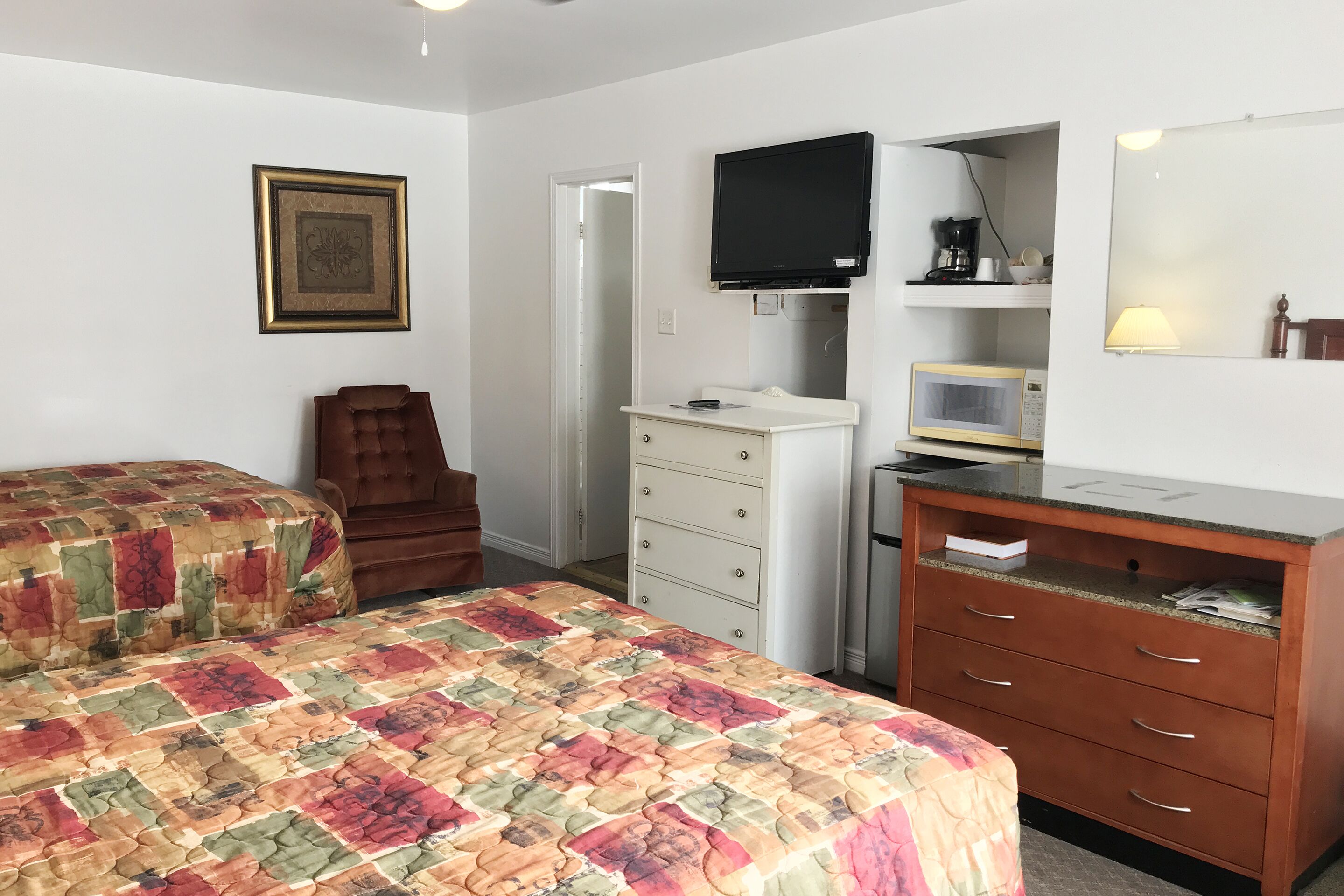 Un dormitorio con dos camas, una silla, un tocador, un televisor, un microondas y un espejo.