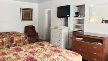 Un dormitorio con dos camas, una silla, un tocador, un televisor, un microondas y un espejo.