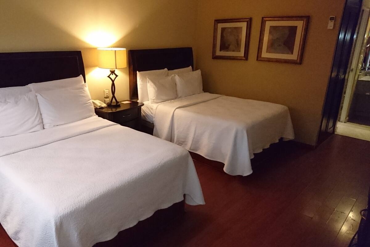 Two single beds with white linens, a bedside table with a lamp, and two framed pictures on the wall.
