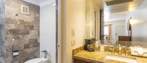 A bathroom with a marble wall, a toilet, a sink with a vanity, and a mirror.