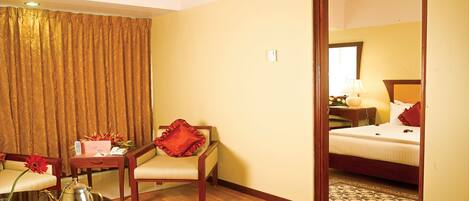 A hotel room with a wooden floor, a bed with white bedding, a red chair, a small table with a teapot and cups, and a mirror reflecting the room.