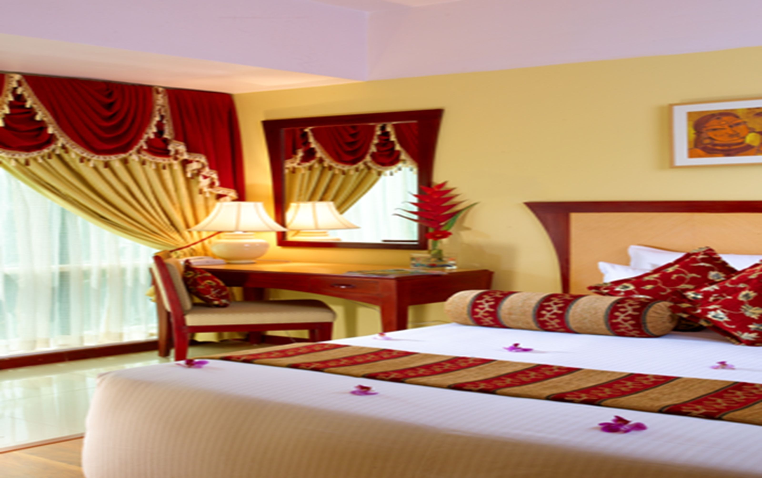 A hotel room with a bed, a desk, a chair, a lamp, and a window with curtains.