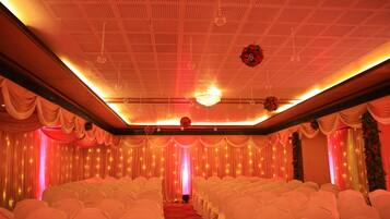 Une salle de banquet avec des rangées de chaises recouvertes de housses blanches, une moquette rouge et des rideaux tombants.