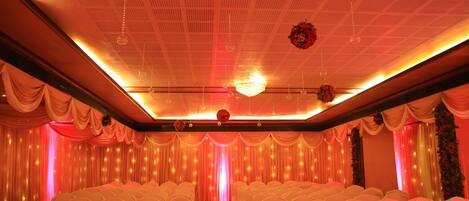 A banquet hall with rows of white-covered chairs, a red carpet, and draped curtains.
