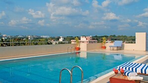 A rooftop pool with clear blue water, a metal ladder, and lounge chairs with striped towels. - Classic Sarovar Portico Thiruvananthapuram (Thiruvananthapuram)