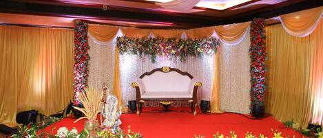 A stage with a white sofa, red carpet, and floral decorations.
