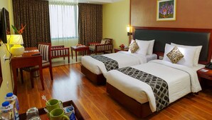 A hotel room with two beds, a desk, a chair, a TV, and a window with curtains. - Classic Sarovar Portico Thiruvananthapuram (Thiruvananthapuram)