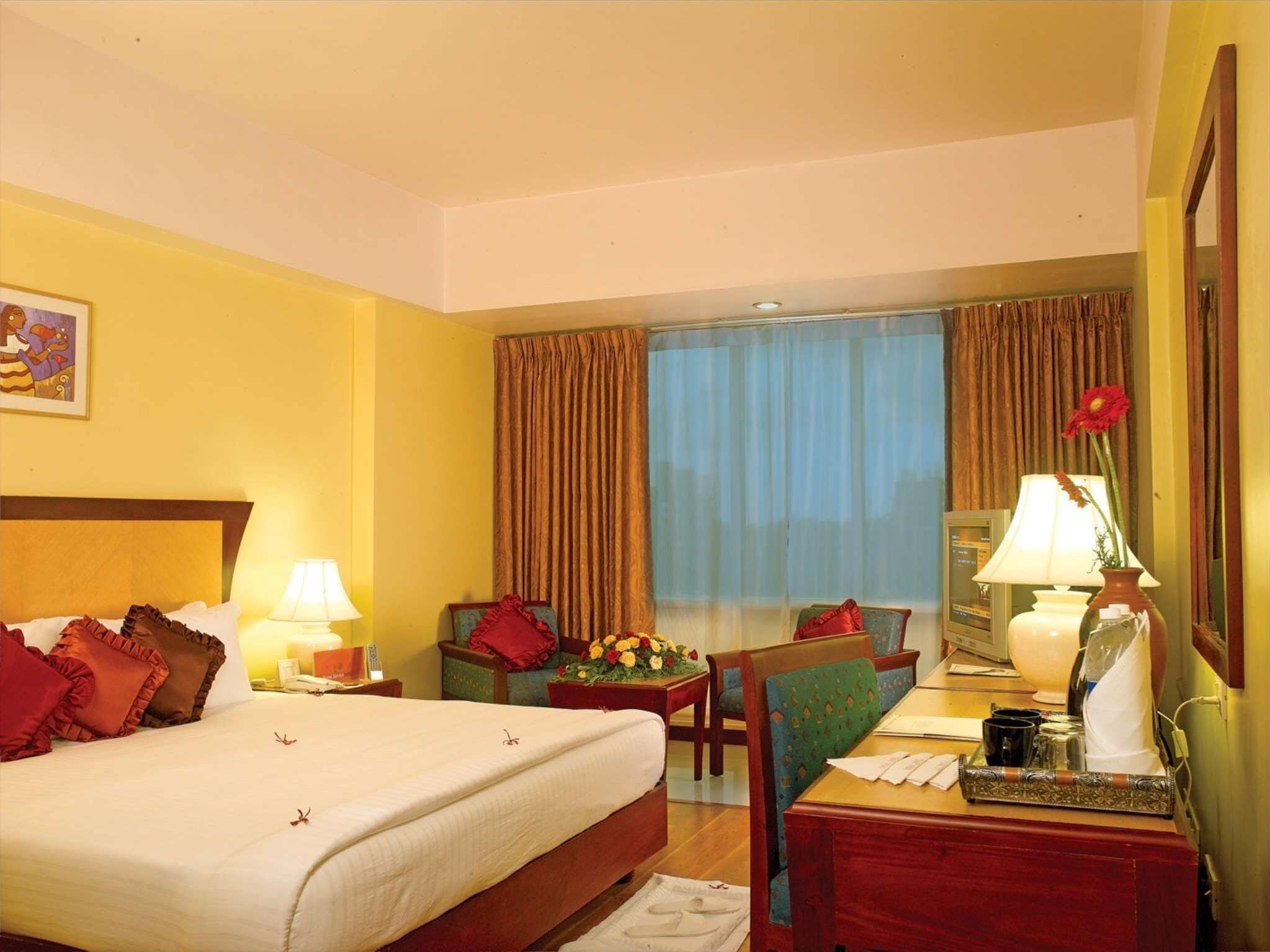 A hotel room with a bed, a desk, a chair, a lamp, and a window with curtains.