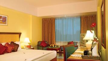 A hotel room with a bed, a desk, a chair, a lamp, and a window with curtains.
