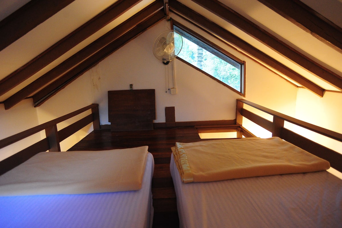 Une chambre avec deux lits, des poutres en bois, une fenêtre et un ventilateur de plafond.